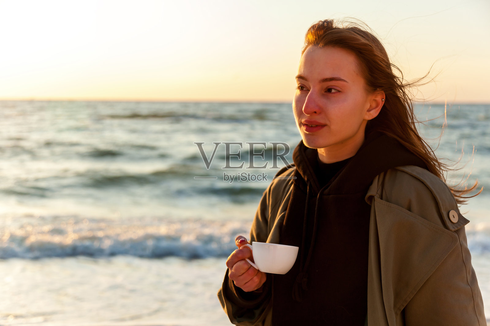 海边日落时分，手握咖啡杯的女人照片摄影图片