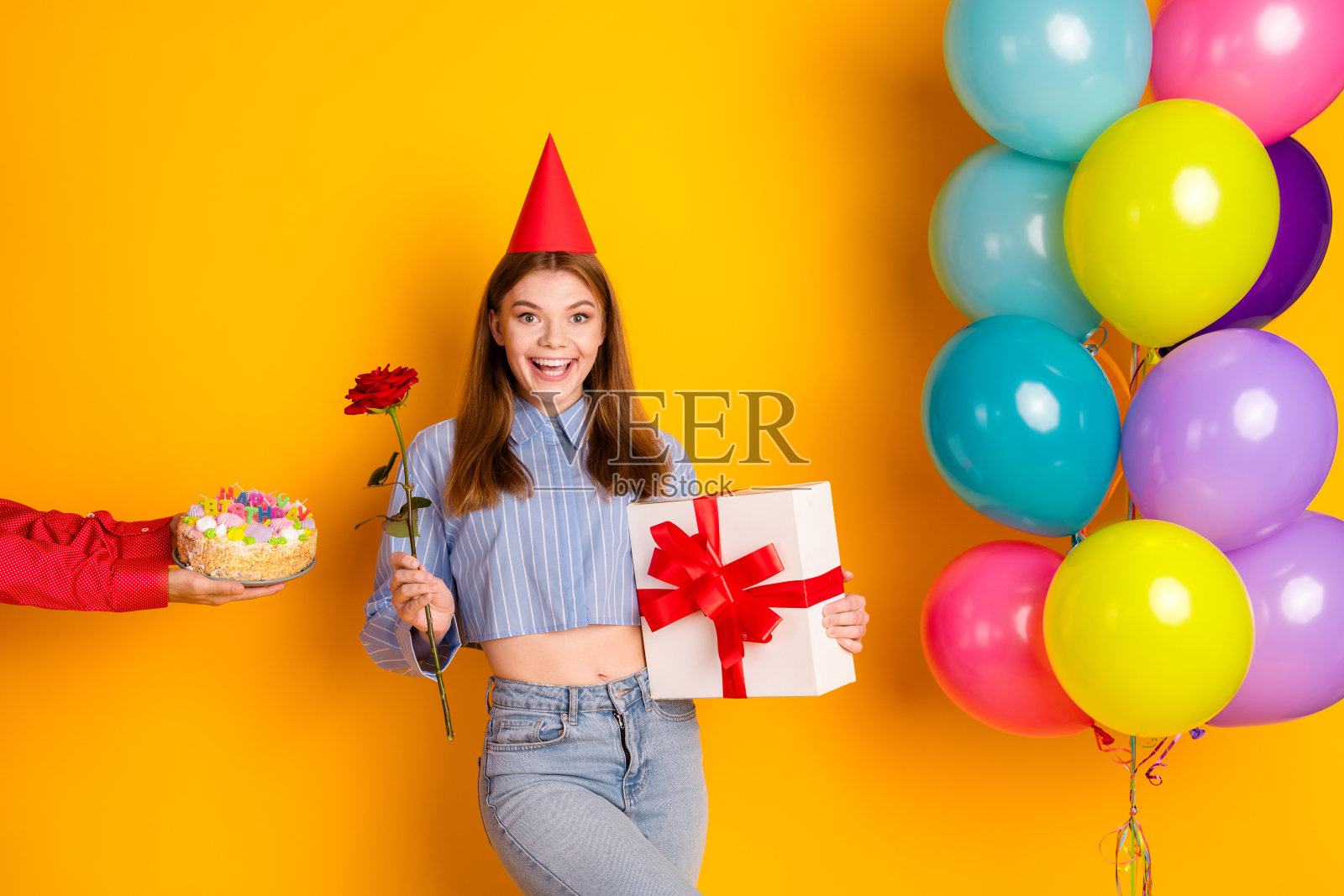 快乐的年轻女性在黄色背景下庆祝生日，周围有气球、礼物和蛋糕，气氛欢快。照片摄影图片