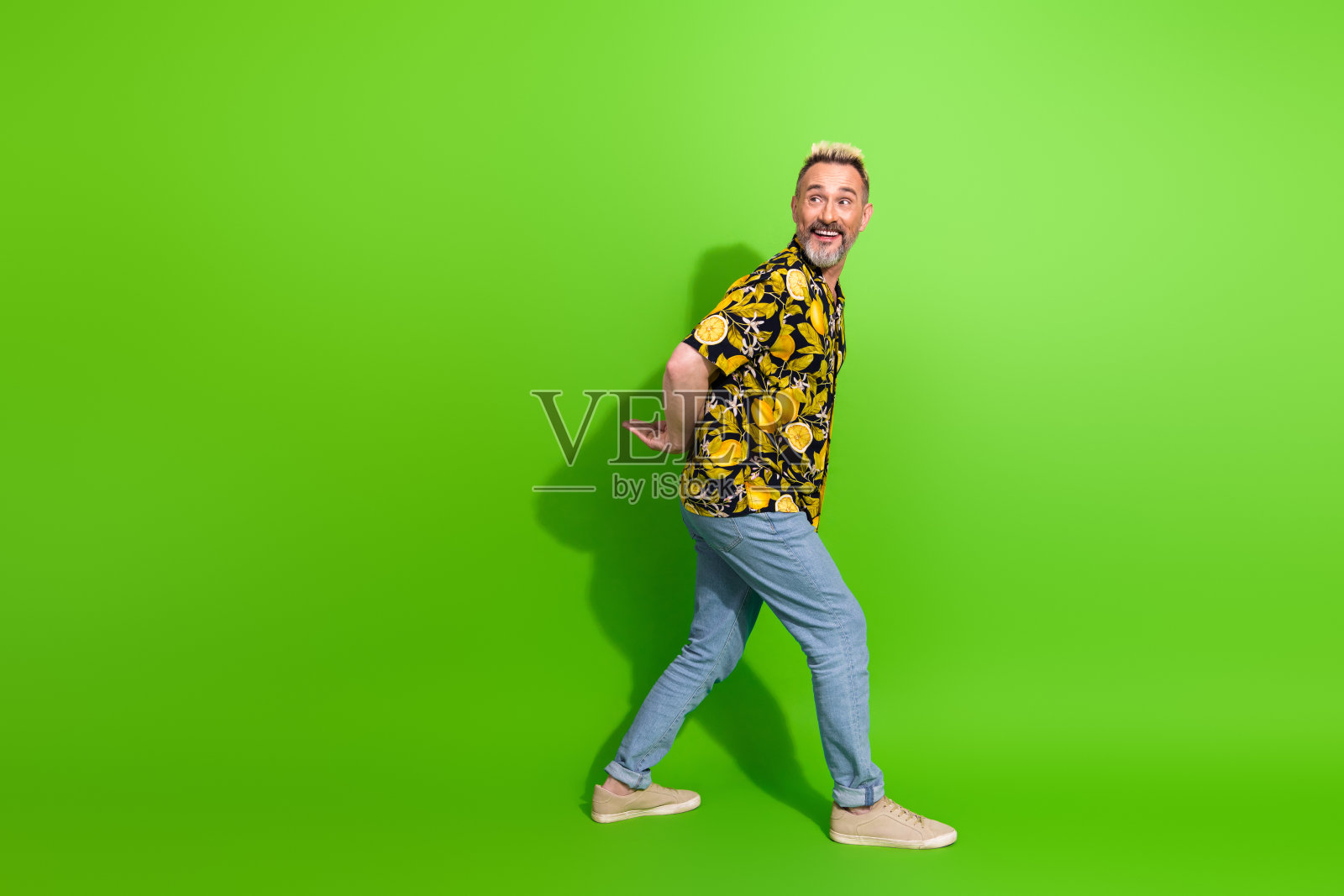 穿着花卉夏威夷衬衫的快乐成熟男性，摆出俏皮的姿势，背景为生机勃勃的绿色。照片摄影图片