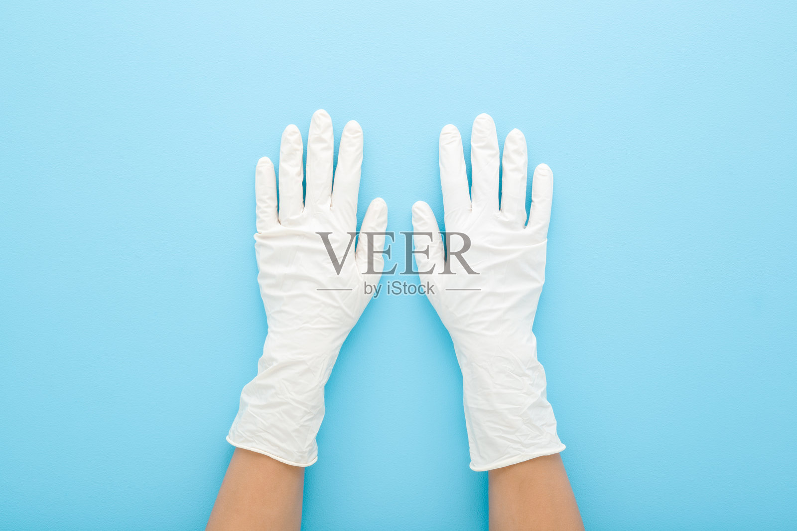 年轻女性的手戴着白色乳胶防护手套，背景为浅蓝色桌面。柔和的色调。特写镜头。俯视角度。照片摄影图片
