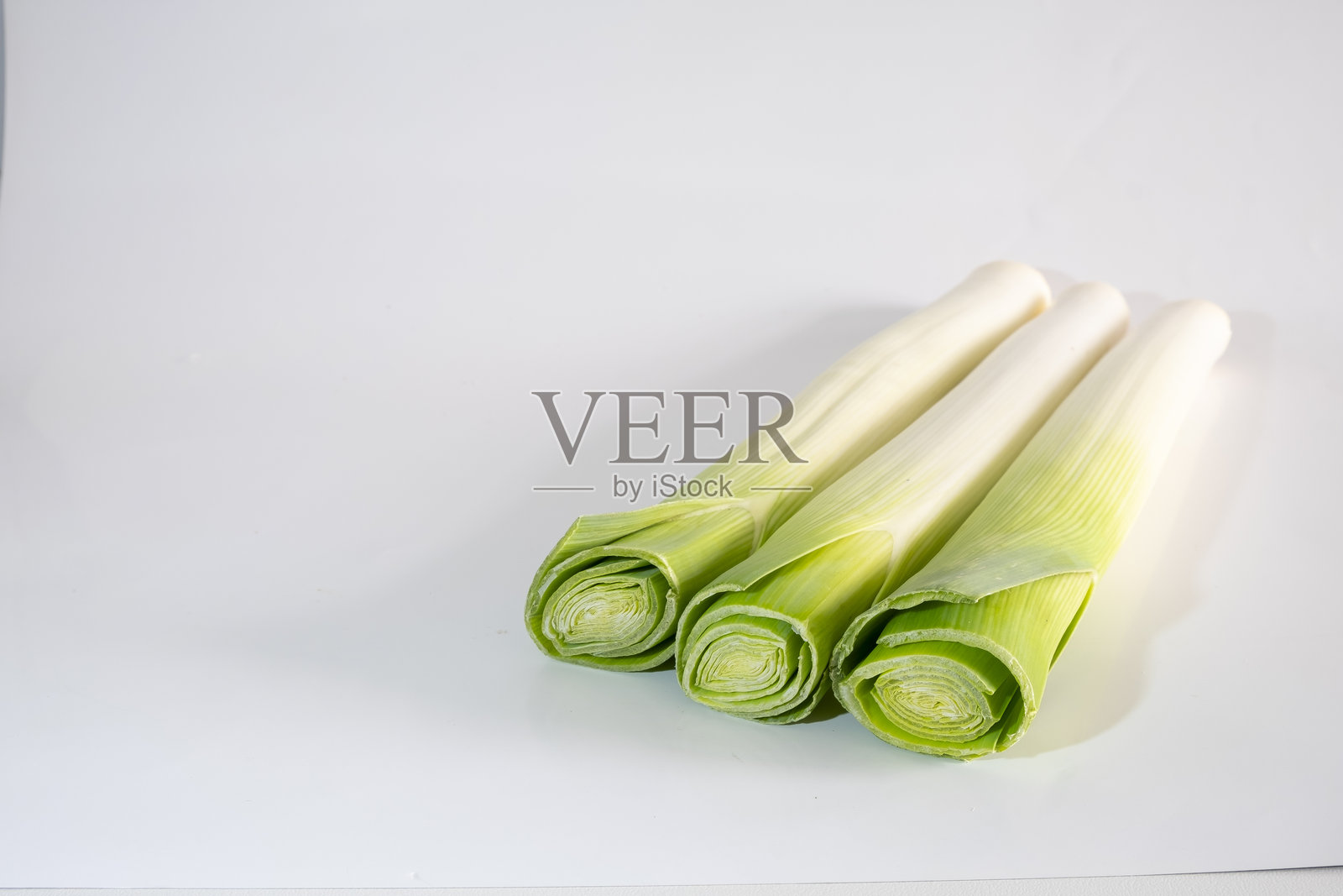 三根新鲜的绿色韭菜，孤立在白色背景上，留有空白空间。大葱（Allium ampeloprasum var. porrum），或称春洋葱，是大葱（Allium ampeloprasum）物种的一个变种。照片摄影图片