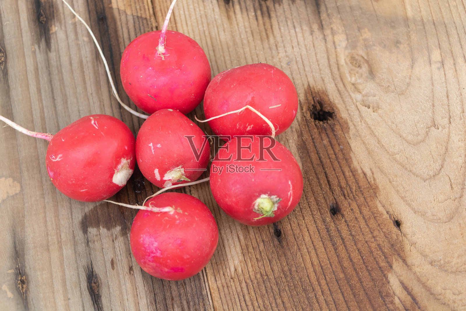 一张俯视图，展示了几颗鲜红的萝卜放在一张古老的木桌上，焦点集中在一颗鲜艳的粉色萝卜上。照片摄影图片