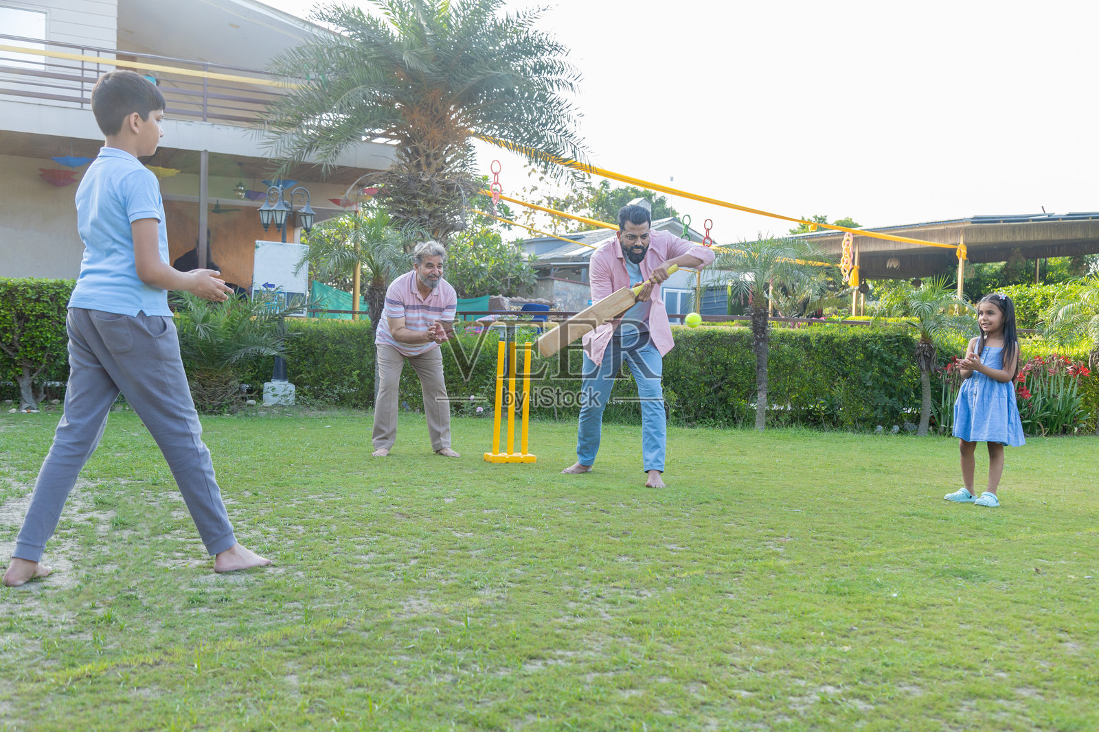 年轻的印度家庭在户外玩板球，父亲和孩子们一起享受野餐游戏。暑假时光。照片摄影图片