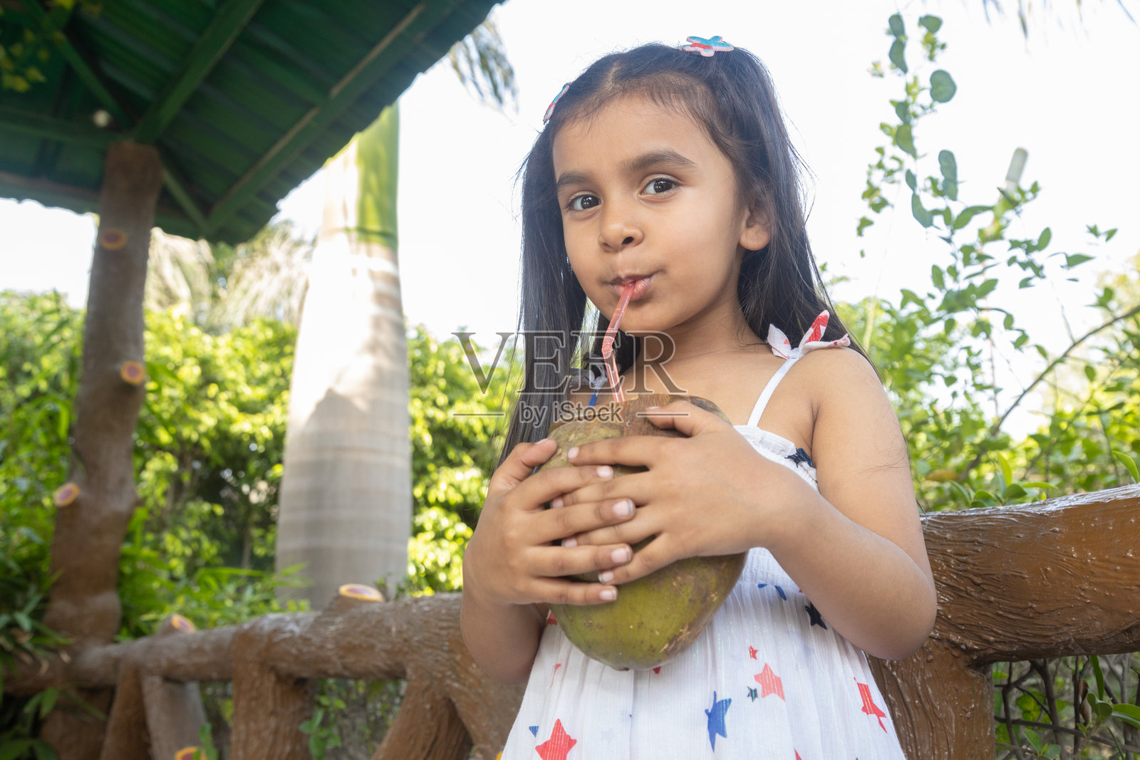 小印度女孩在夏季享受椰子水。孩子在喝健康饮品，童年。照片摄影图片