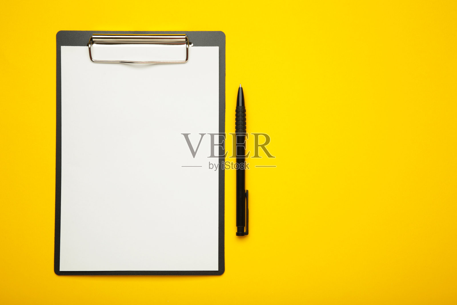 黑色平板电脑上放着一张空白纸和一支笔，背景为黄色。留有文本空间。照片摄影图片