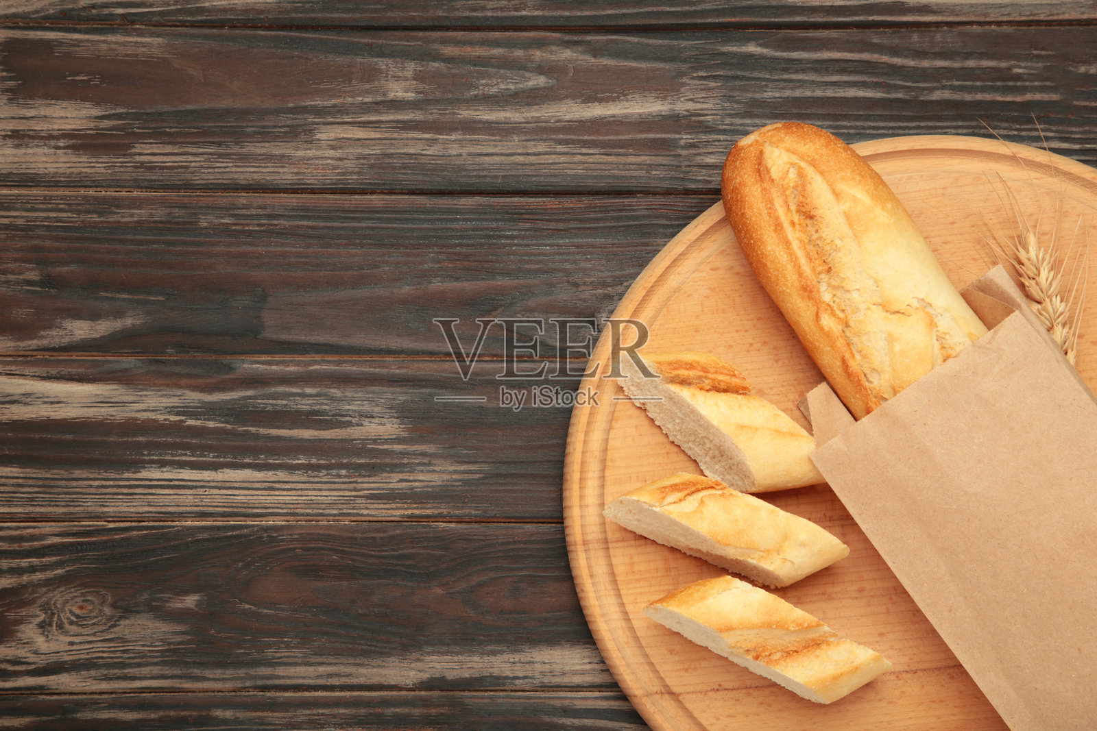 整根法棍和切成块的法棍放在棕色背景的切菜板上照片摄影图片