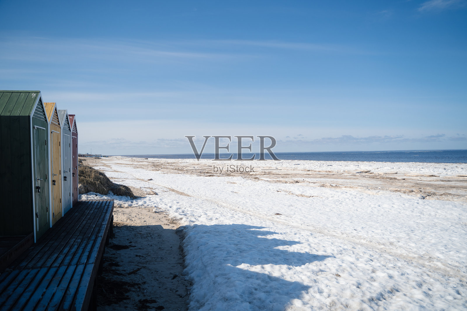 阳光明媚的寒冷北海，沙滩上部分融化了冬季的雪和冰，岸边有五彩斑斓的木屋。照片摄影图片