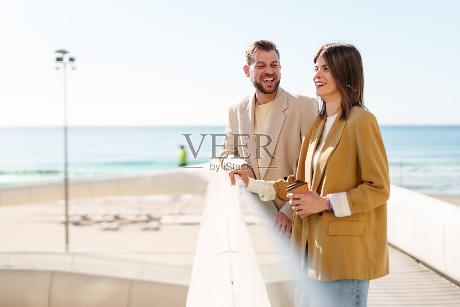 穿着时尚西装的职业情侣在阳光明媚的海滨步道上共享咖啡时光照片摄影图片