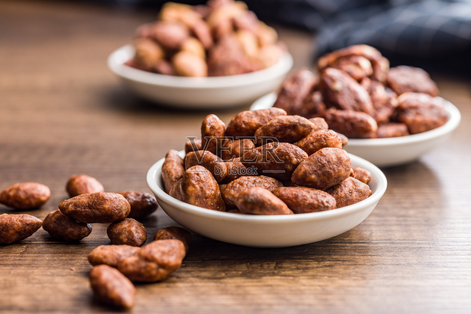 碗里装着糖和蜂蜜裹的杏仁，放在木桌上。照片摄影图片