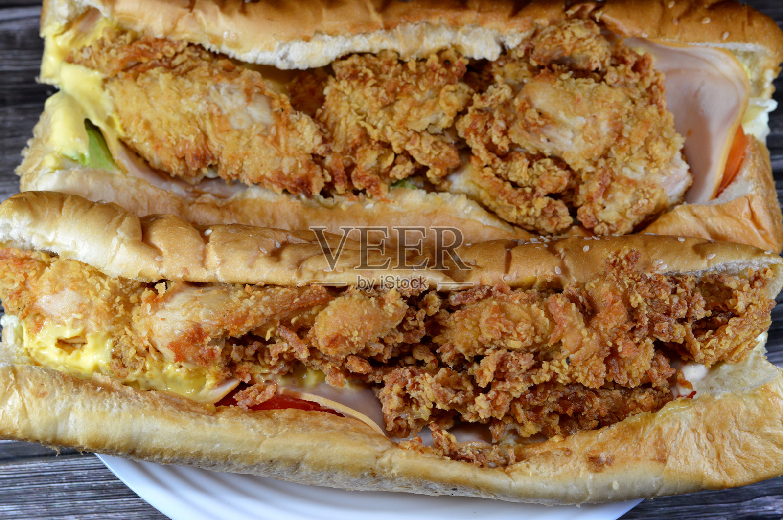 炸鸡脆皮块配烟熏火鸡片、生菜、番茄、切达奶酪和美味酱，夹在撒有芝麻的长面包中，西式三明治内填满鸡肉块。照片摄影图片