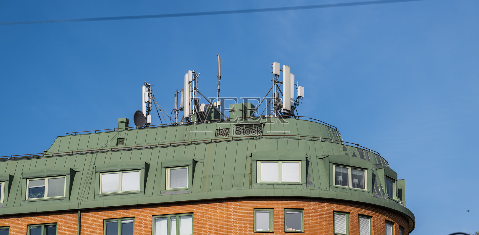 带有多个天线的绿顶砖建筑。照片摄影图片