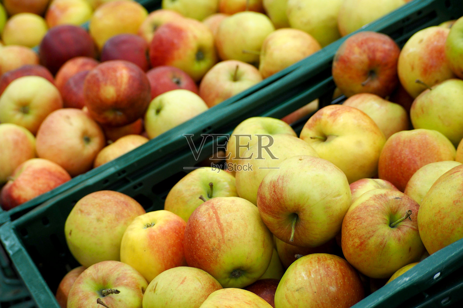 绿色塑料箱中装满了许多黄色苹果。超市侧面视图。照片摄影图片