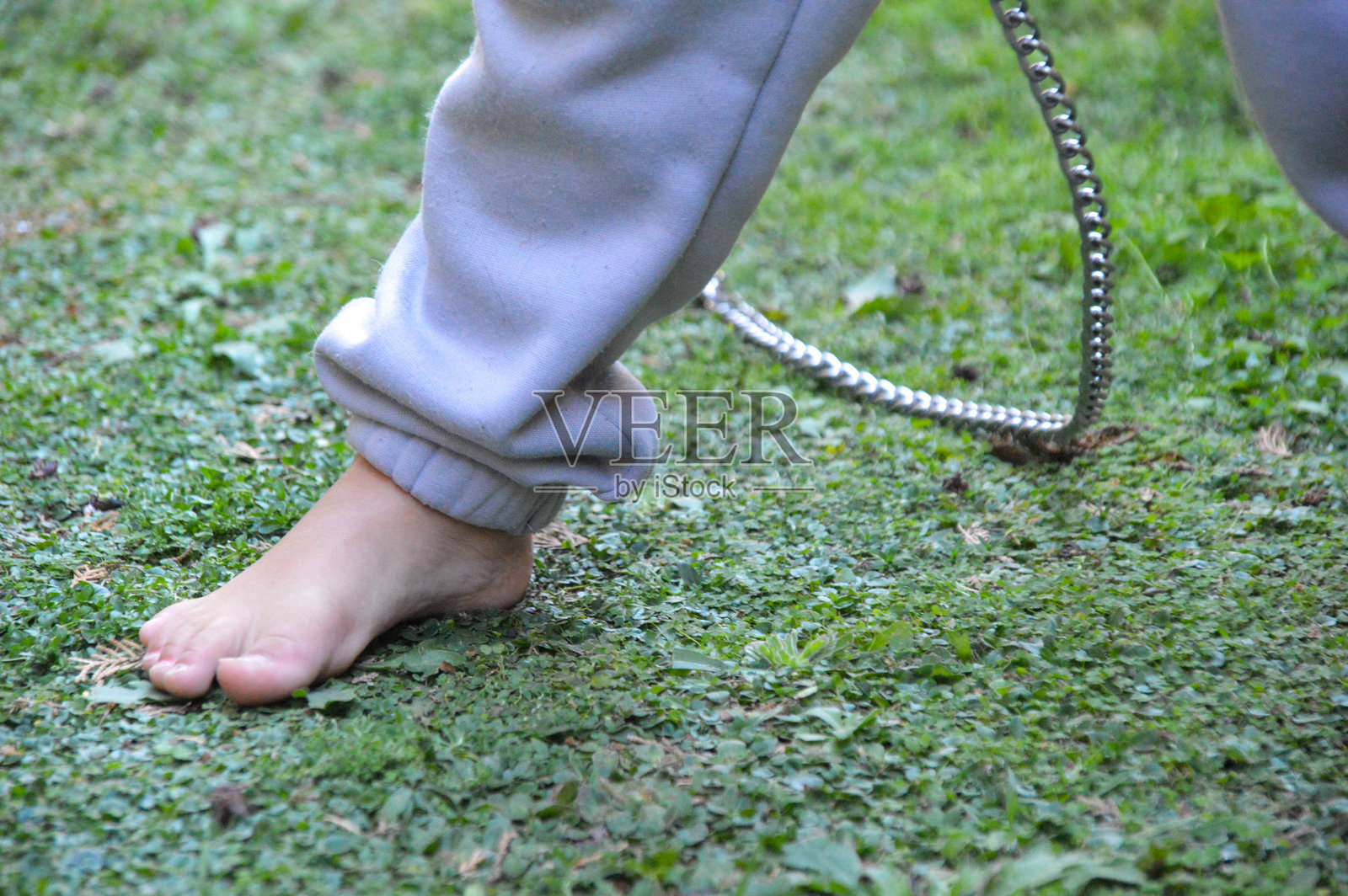 白人儿童赤脚穿着灰色运动服和金属链条照片摄影图片