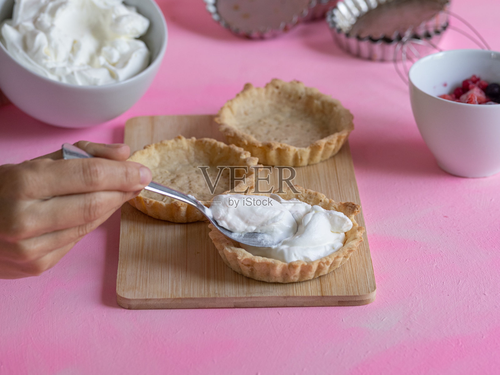 女人的手在一些手工塔里放入奶油。甜点的制作过程。照片摄影图片