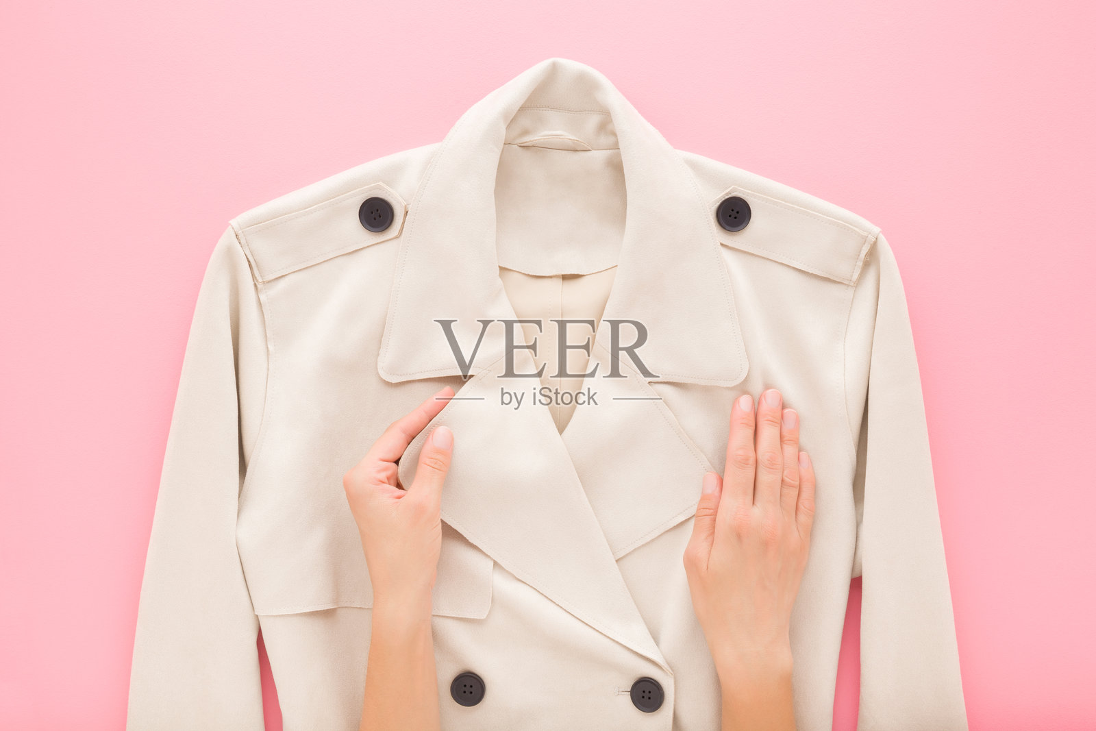 年轻女性的手触摸着新款柔软的米色外套，背景为浅粉色桌面。柔和的色调。视角拍摄。特写。女性优雅的服装。俯视图。照片摄影图片