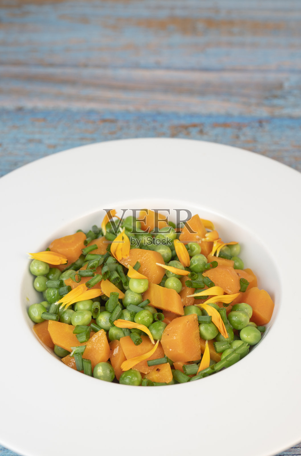 新鲜的花园豌豆和胡萝卜用黄油烹饪，点缀细香葱和万寿菊花，成为一道色彩鲜艳的配菜。照片摄影图片