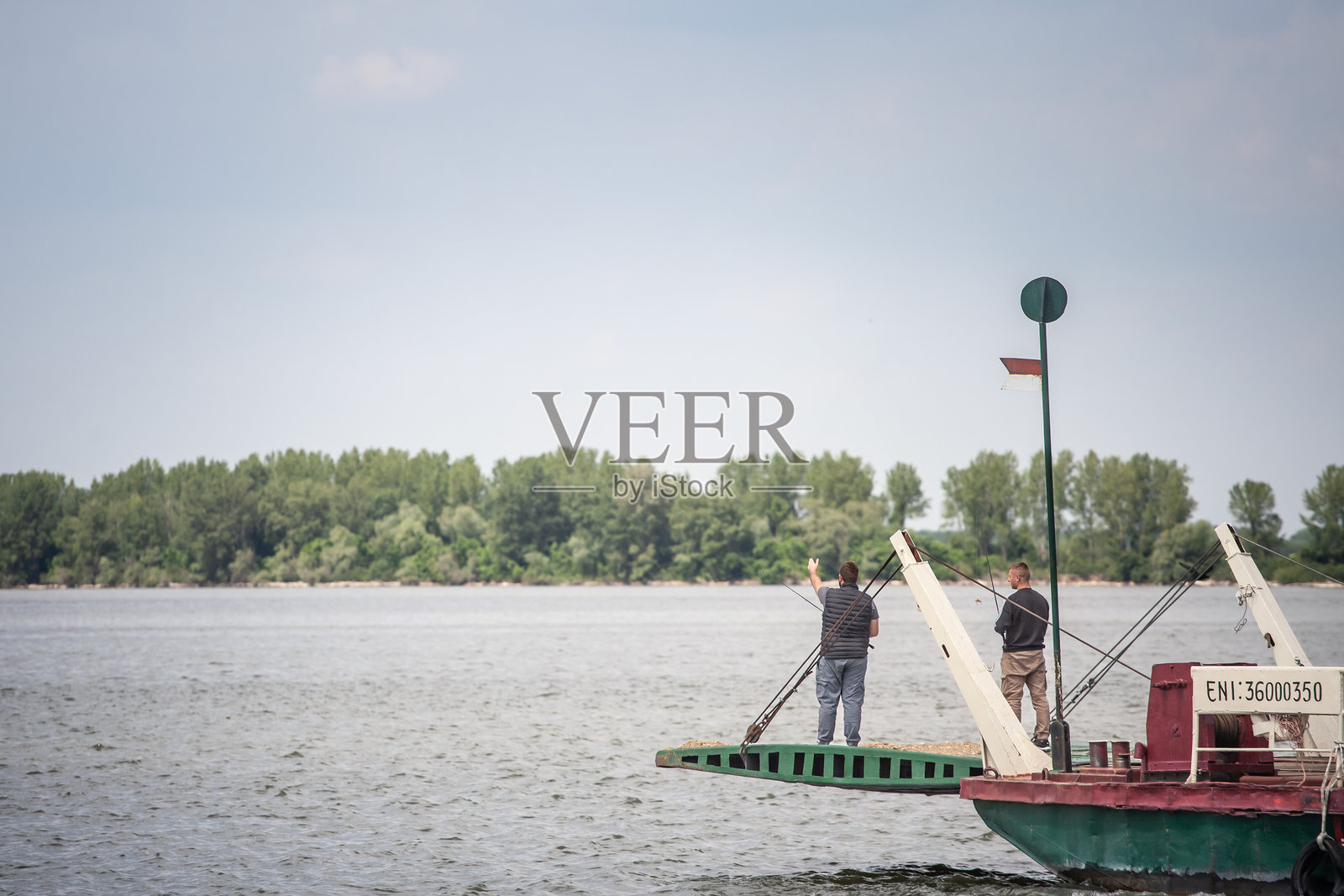 在塞尔维亚的拉姆，铁门附近的多瑙河上，两位渔民在渡船上钓鱼，春天的选择性模糊效果。照片摄影图片