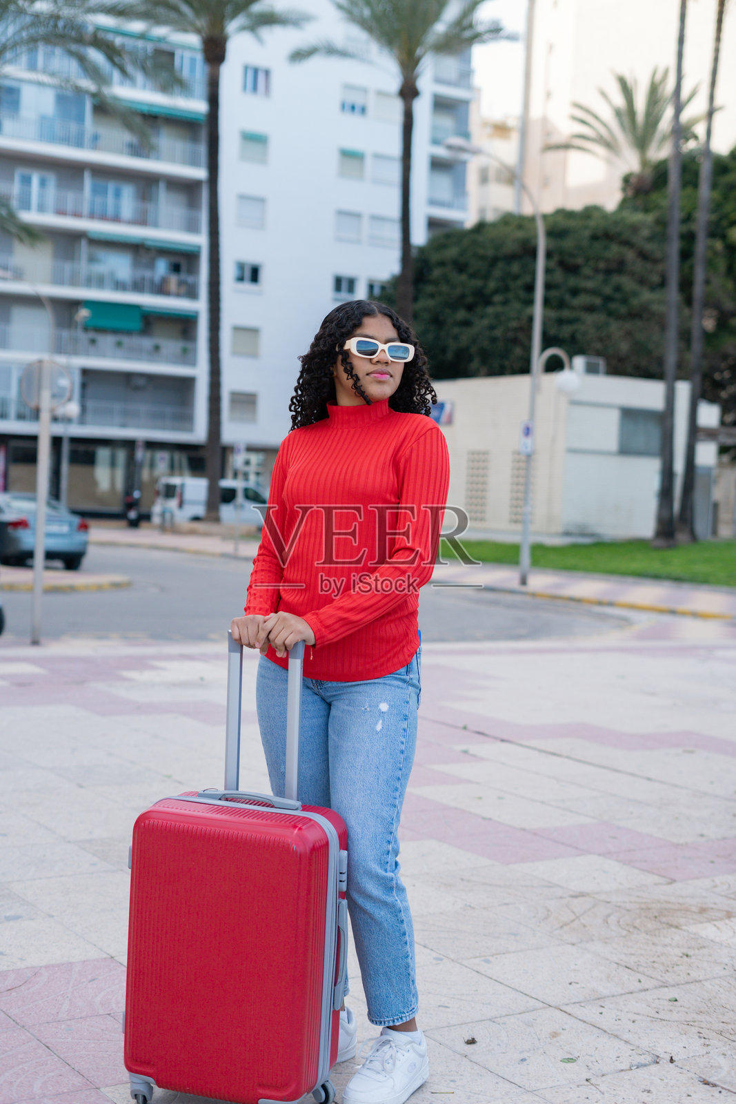 年轻的女游客在城市中拖着她的红色行李箱。照片摄影图片