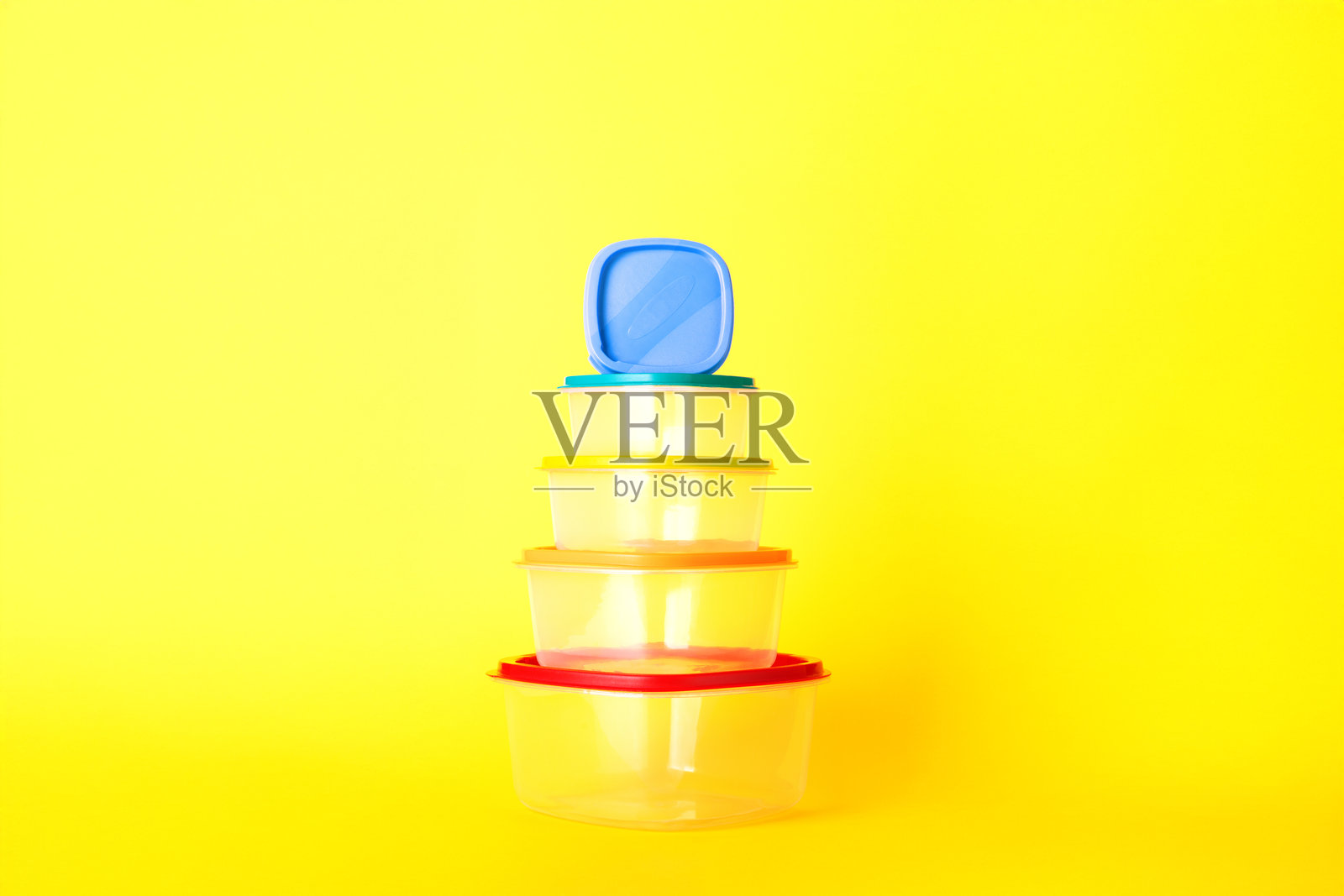 透明塑料容器，五颜六色的盖子堆成金字塔形，顶部盖子倾斜，背景为明亮的黄色。照片摄影图片