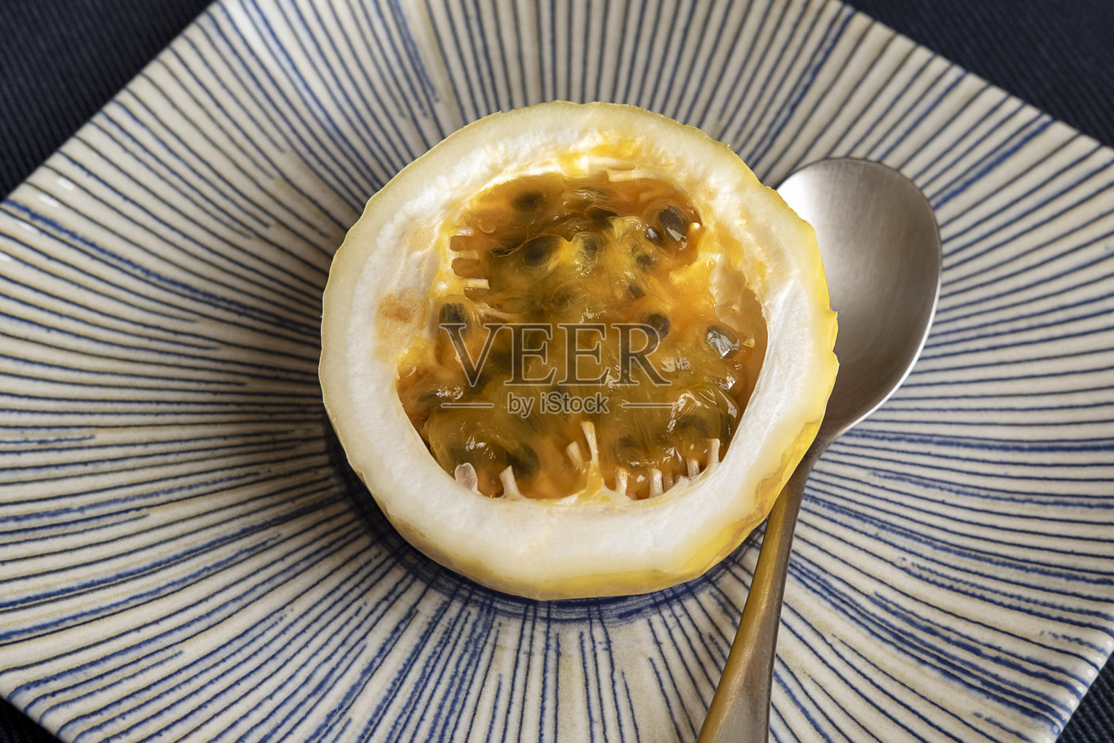 切开的百香果展示出金色果肉和闪亮的种子，放在带有放射状蓝色图案的陶瓷盘上。照片摄影图片