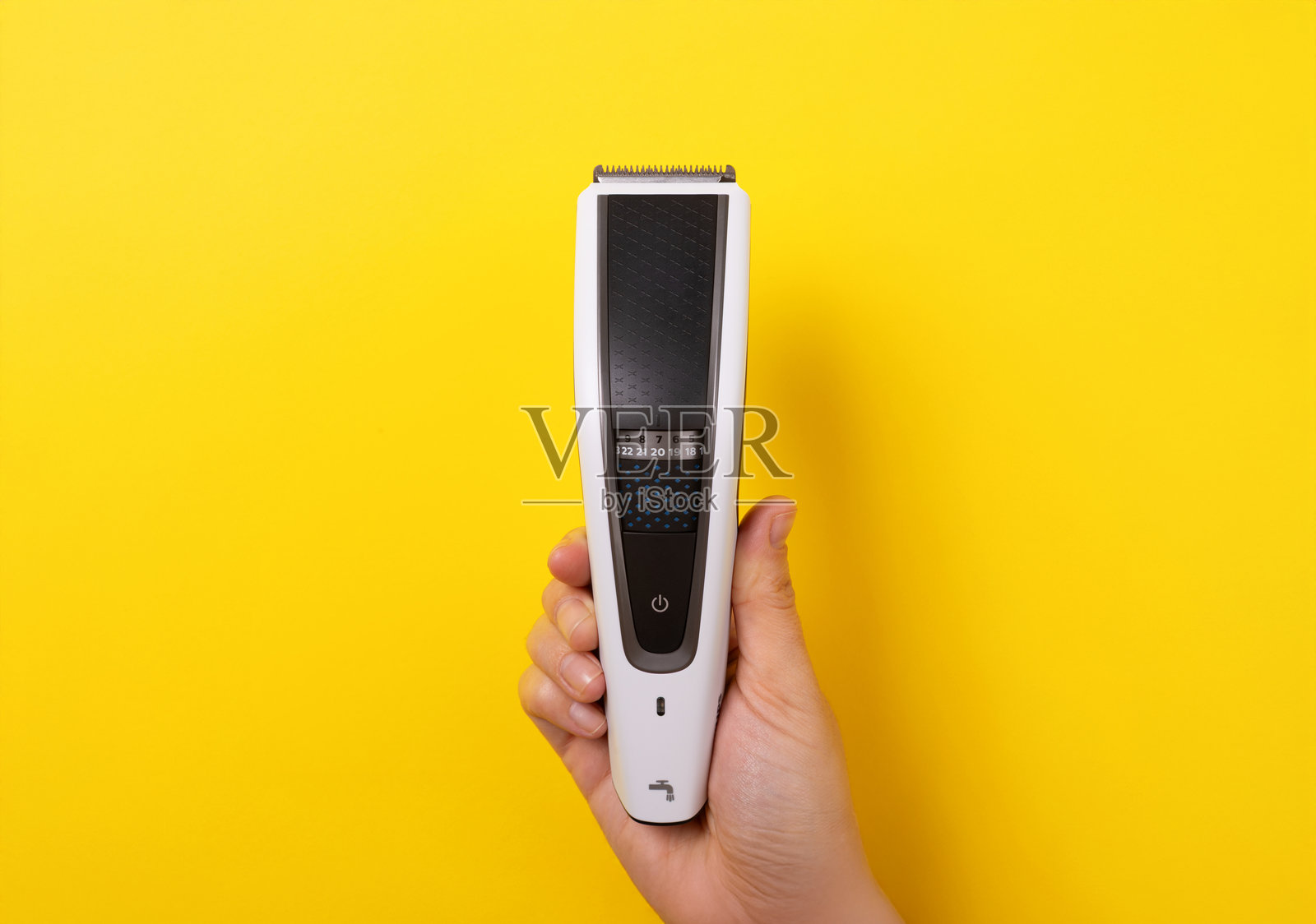 手握现代电动理发器，垂直放置于纯黄色背景前，体现美容概念。照片摄影图片