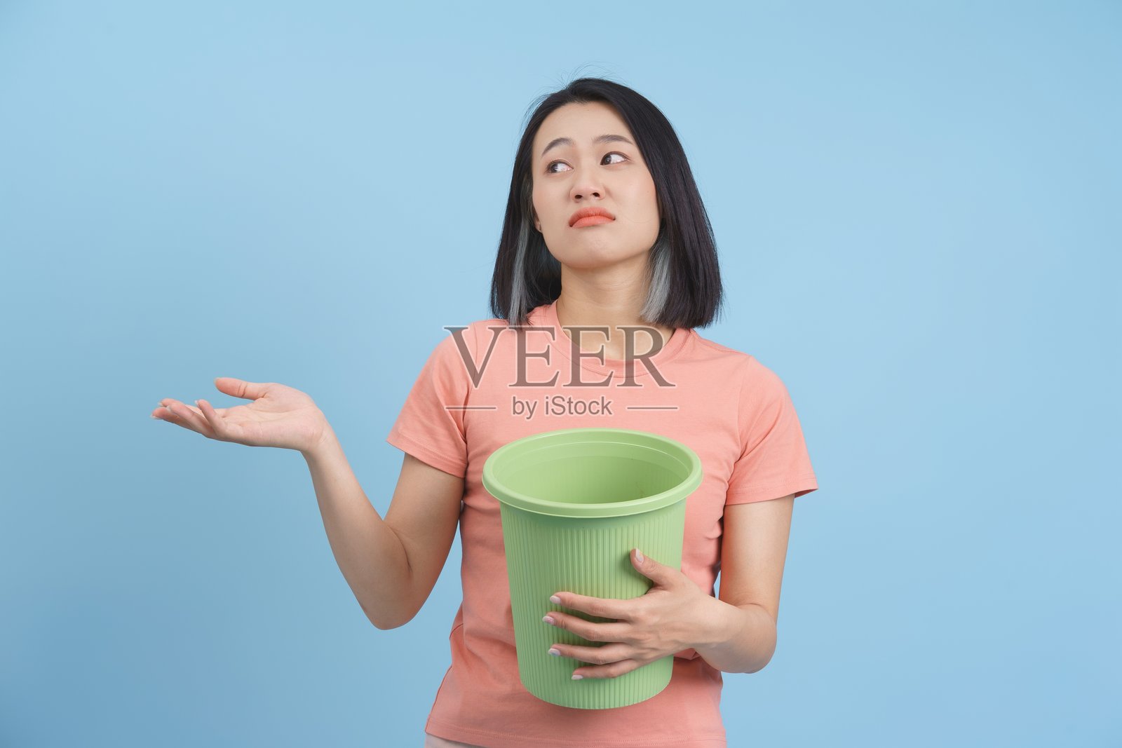 蓝色背景下，女人抱着垃圾桶耸肩照片摄影图片