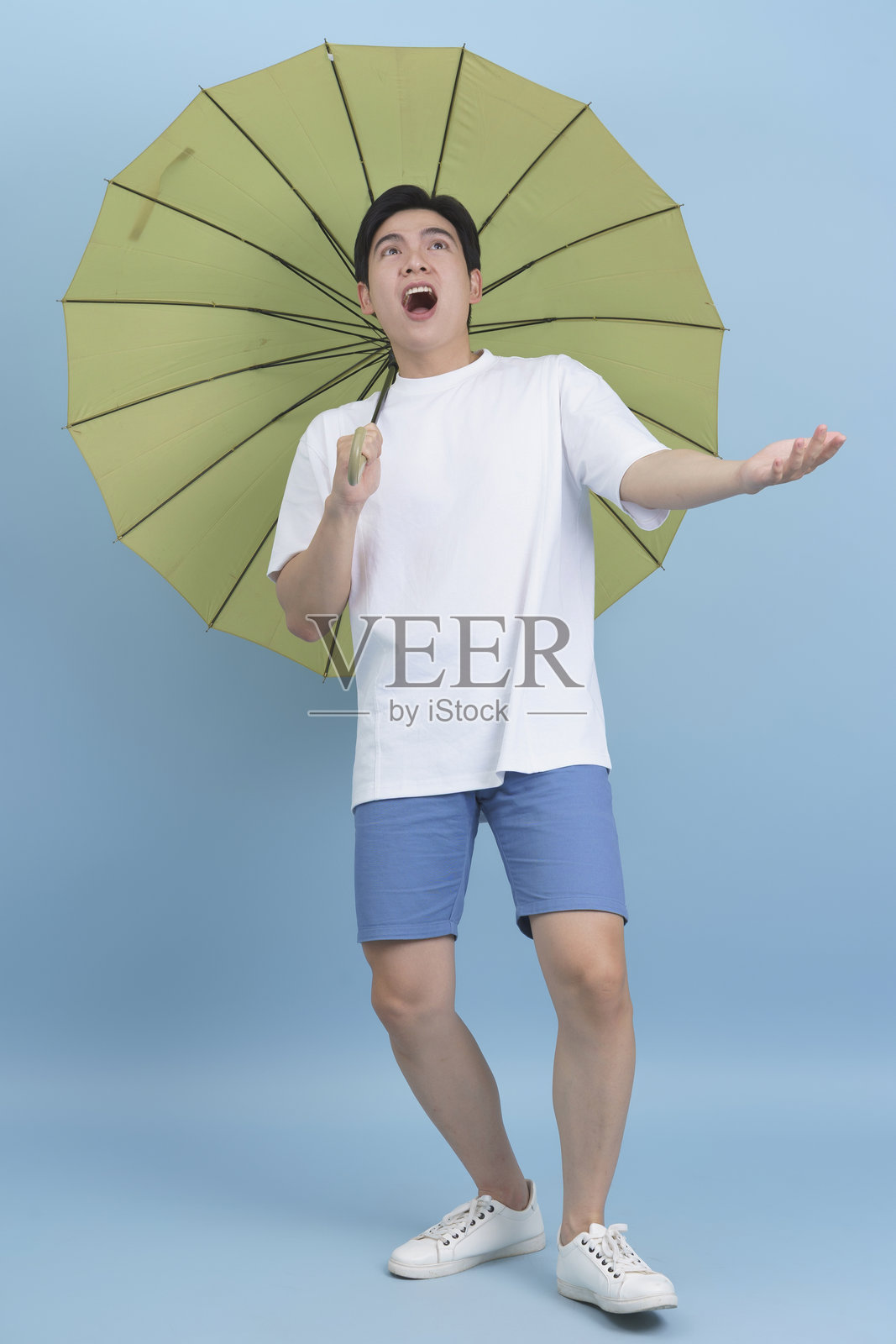 兴奋的年轻男子手持绿色雨伞，背景为蓝色。照片摄影图片