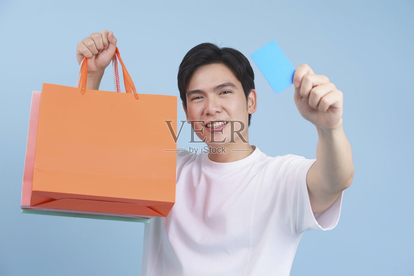 微笑的年轻男子手持购物袋和信用卡，背景为蓝色照片摄影图片