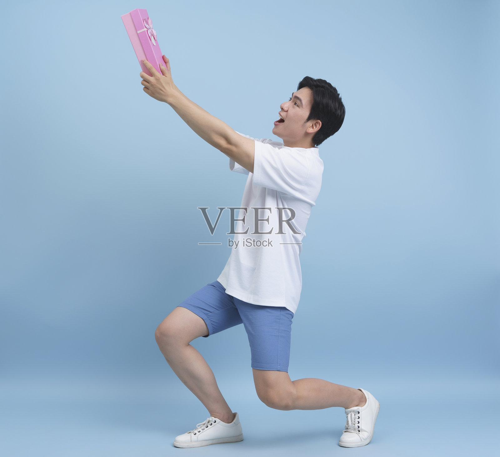 男子跪下在浅蓝色背景前呈现礼物照片摄影图片