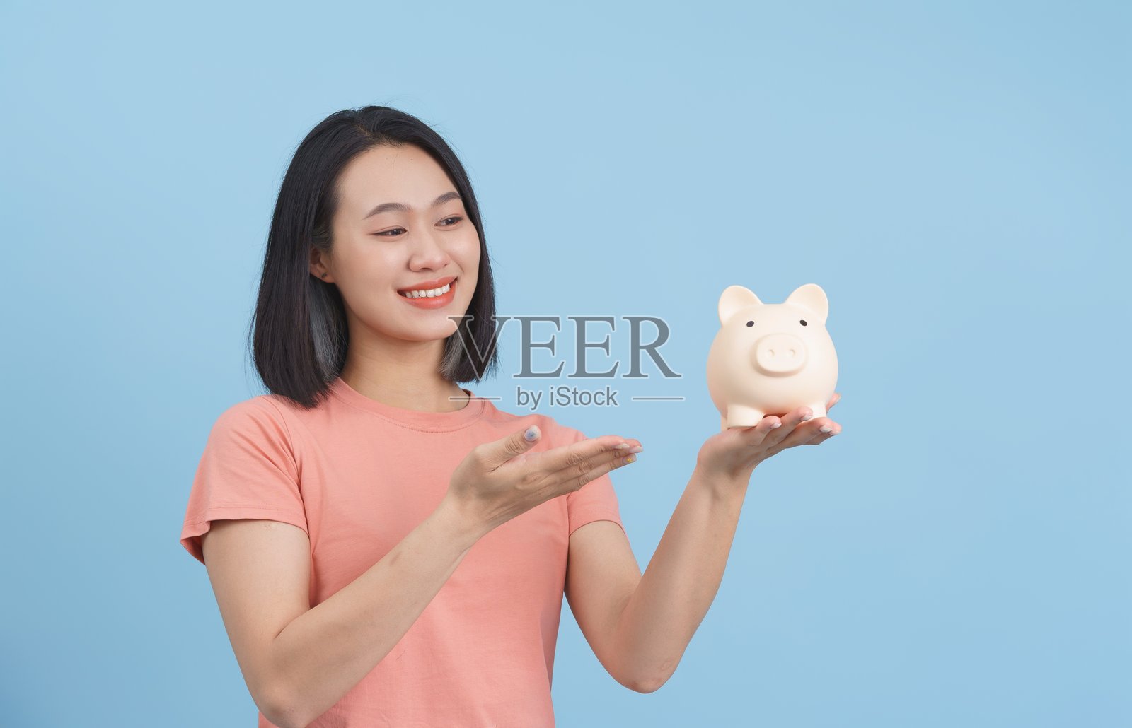 微笑的女性手持储蓄罐，背景为浅蓝色照片摄影图片