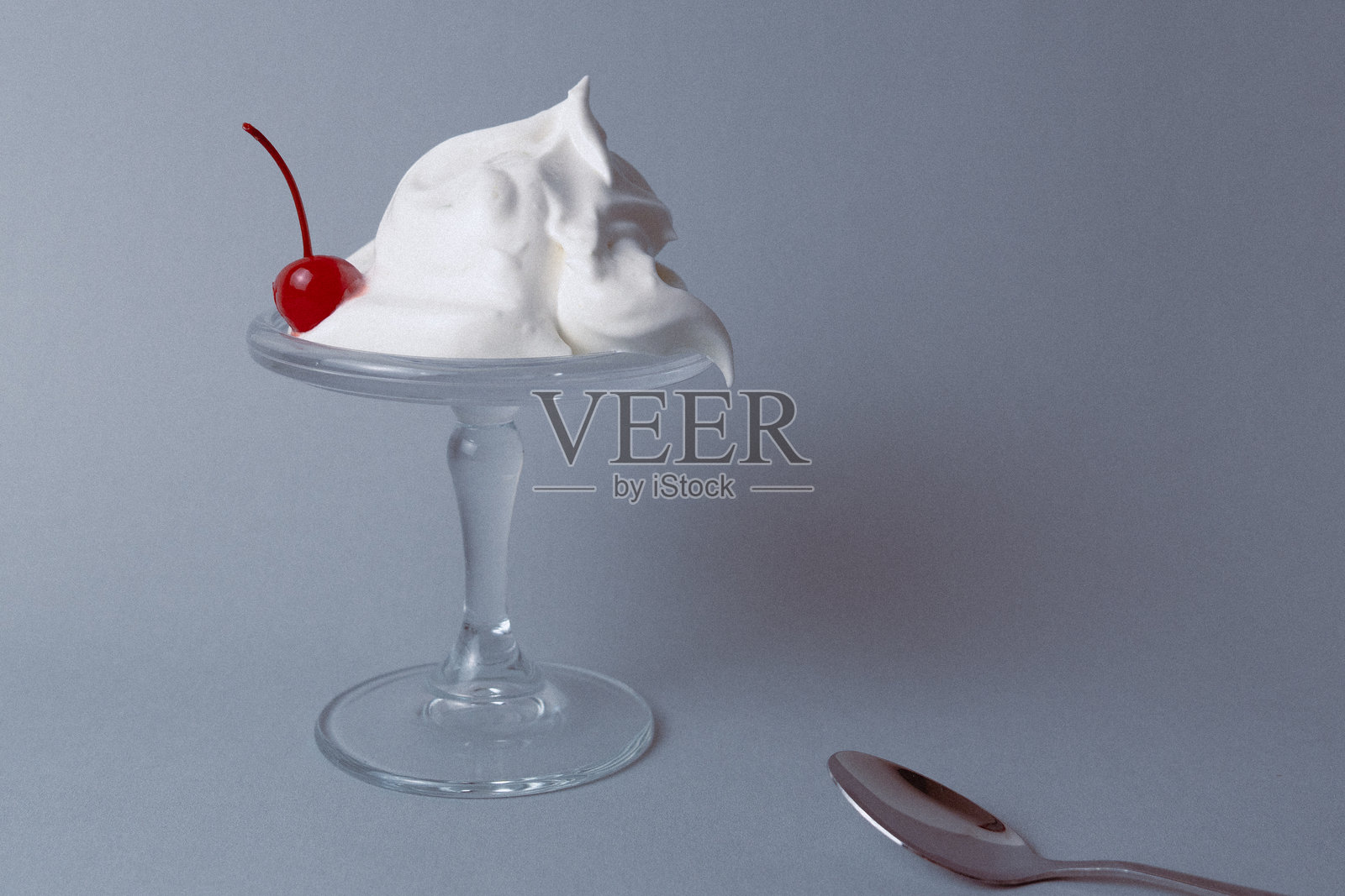 用玻璃高脚杯盛装的鲜奶油甜点，上面点缀着一颗樱桃照片摄影图片