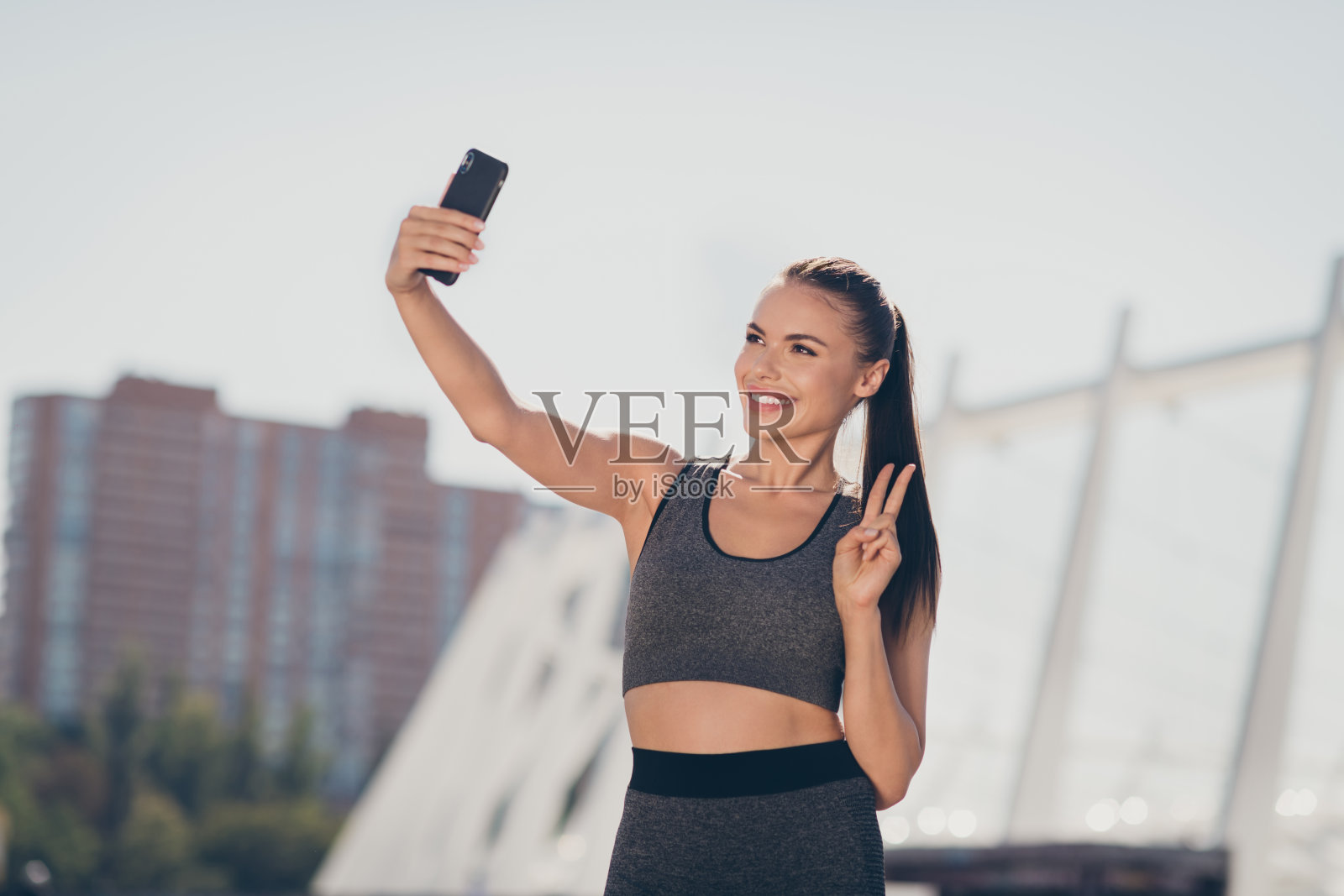 运动教练女士在户外用智能设备录制视频自拍，做出V字手势向博客粉丝打招呼。照片摄影图片