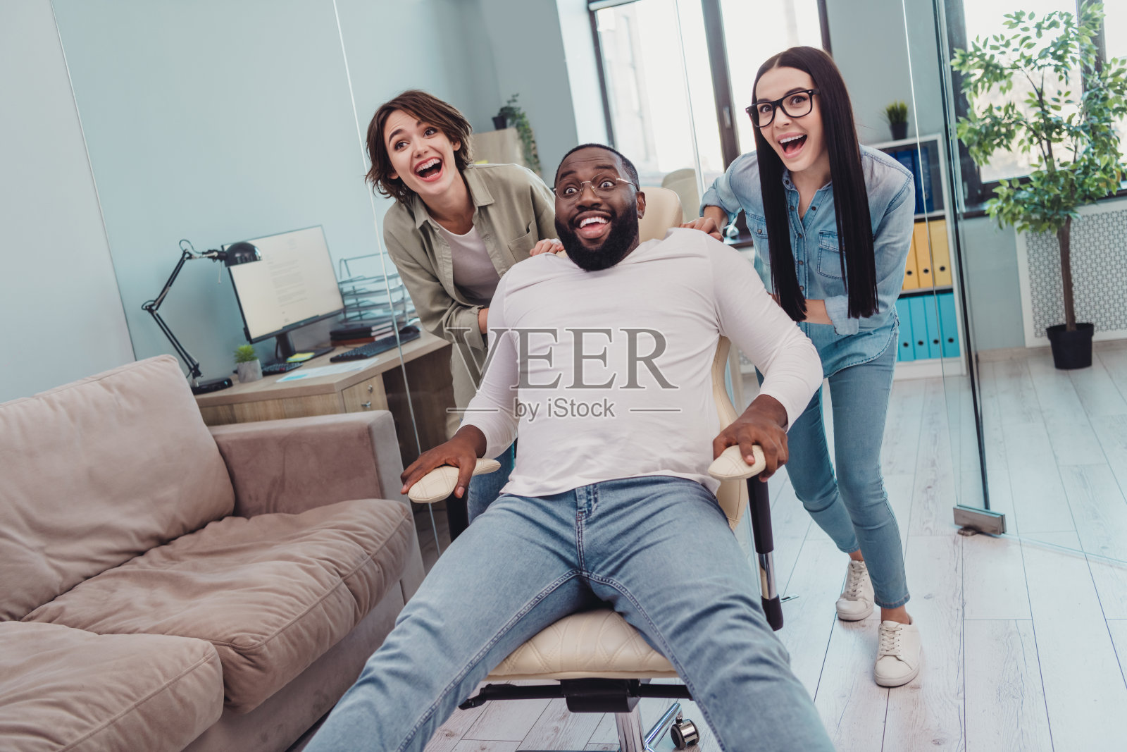 快乐的公司代表在现代工作空间中放松休息，女士们骑在椅子上，男士们快速大喊。照片摄影图片