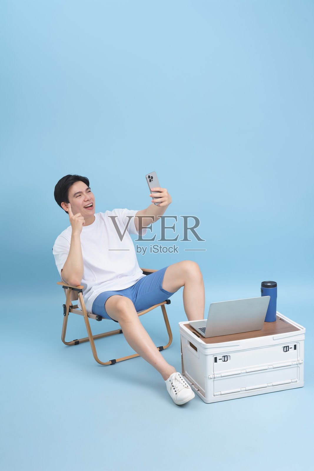 坐在椅子上的男人享受手机视频通话，旁边放着笔记本电脑，轻松自在。照片摄影图片