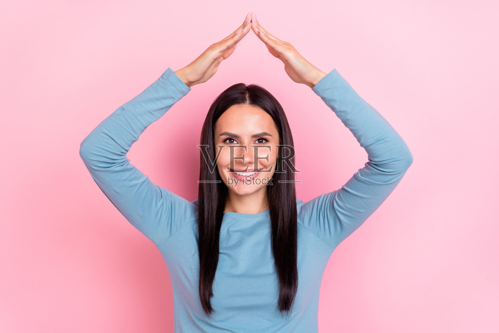 可爱的搞笑女士穿着蓝色衬衫，微笑着展示手臂，背景为粉色。照片摄影图片