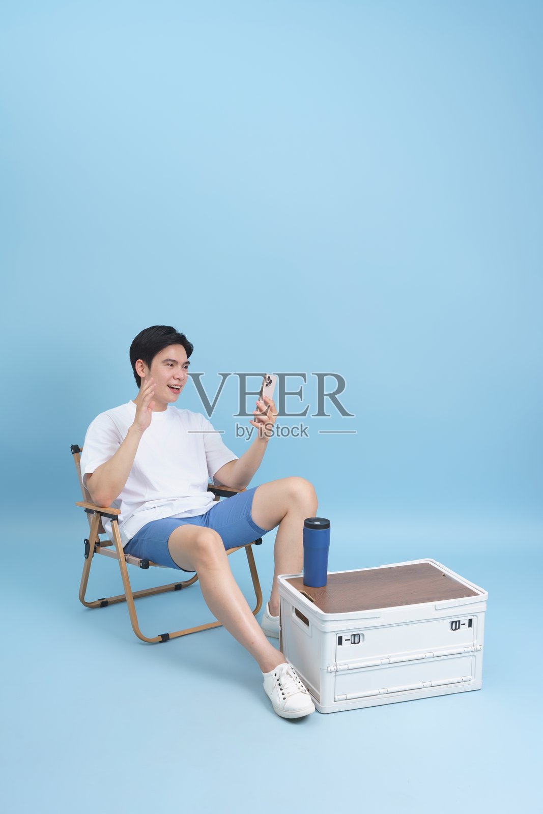 男子在蓝色背景环境中放松地坐在椅子上使用智能手机照片摄影图片