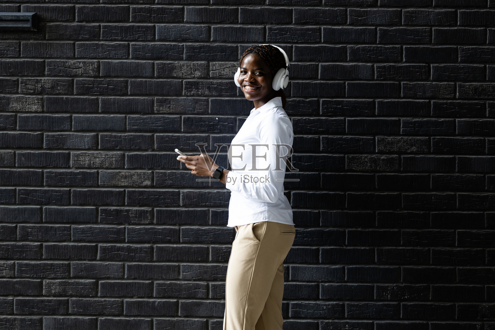 年轻的现代黑人女性手持智能手机，正在听音乐。照片摄影图片