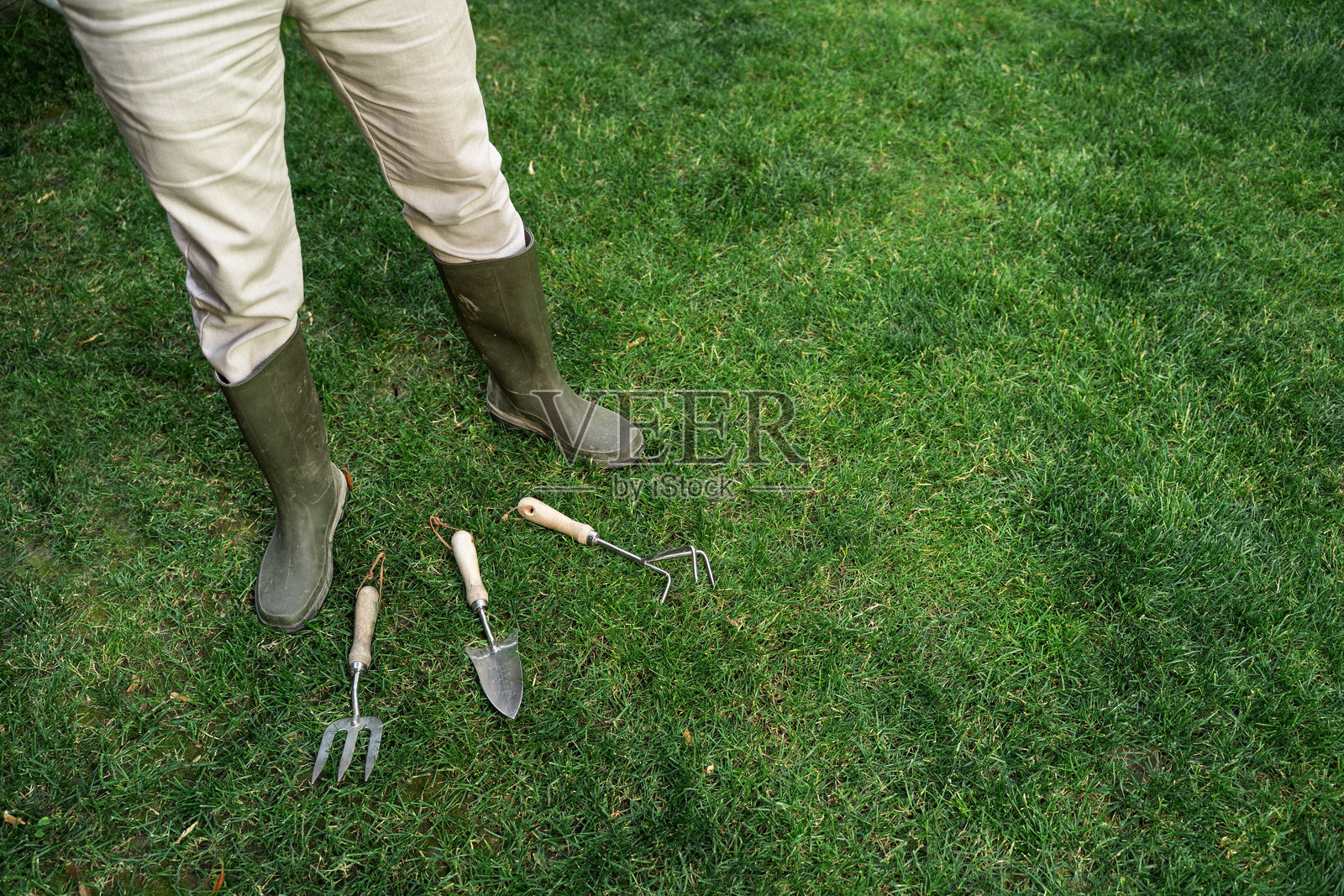 园艺概念，园丁的腿和靴子站在草地上，周围有工具照片摄影图片