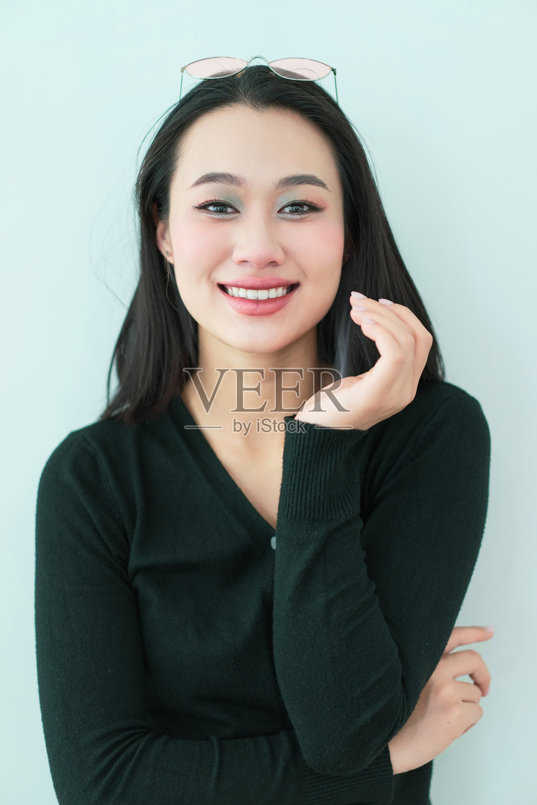 微笑的女性将眼镜戴在头上，摆姿势于简单的浅色背景前照片摄影图片