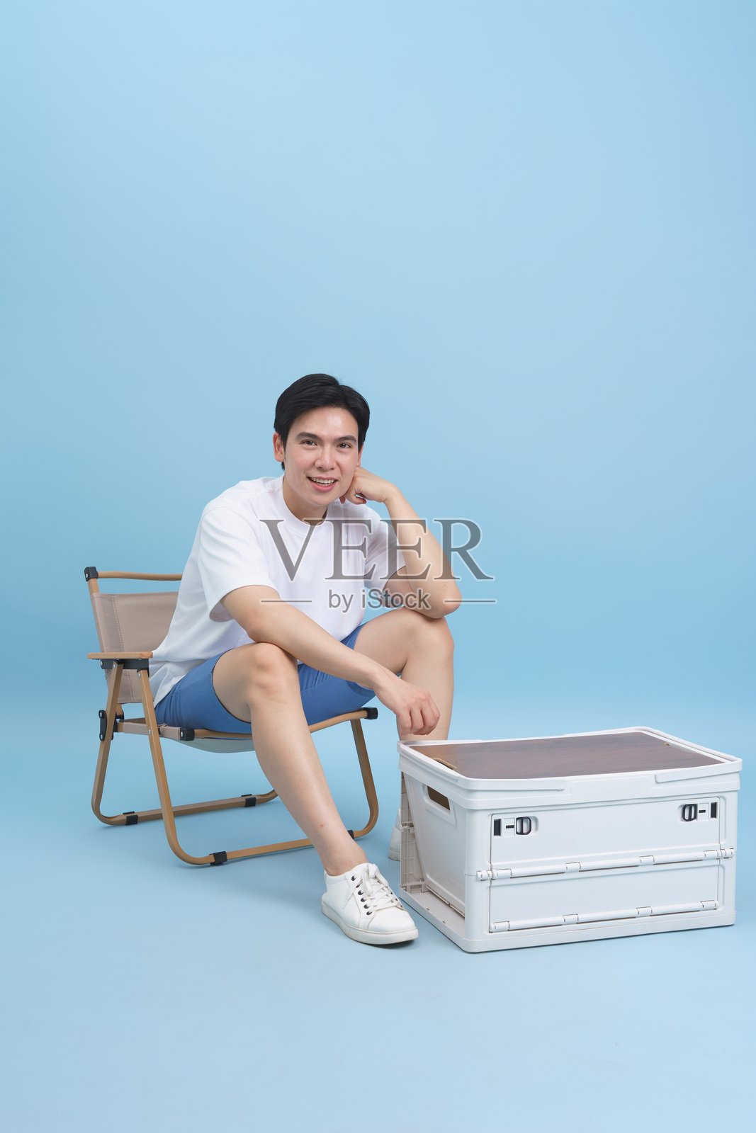 微笑的男人坐在蓝色背景下的折叠椅和桌子旁照片摄影图片