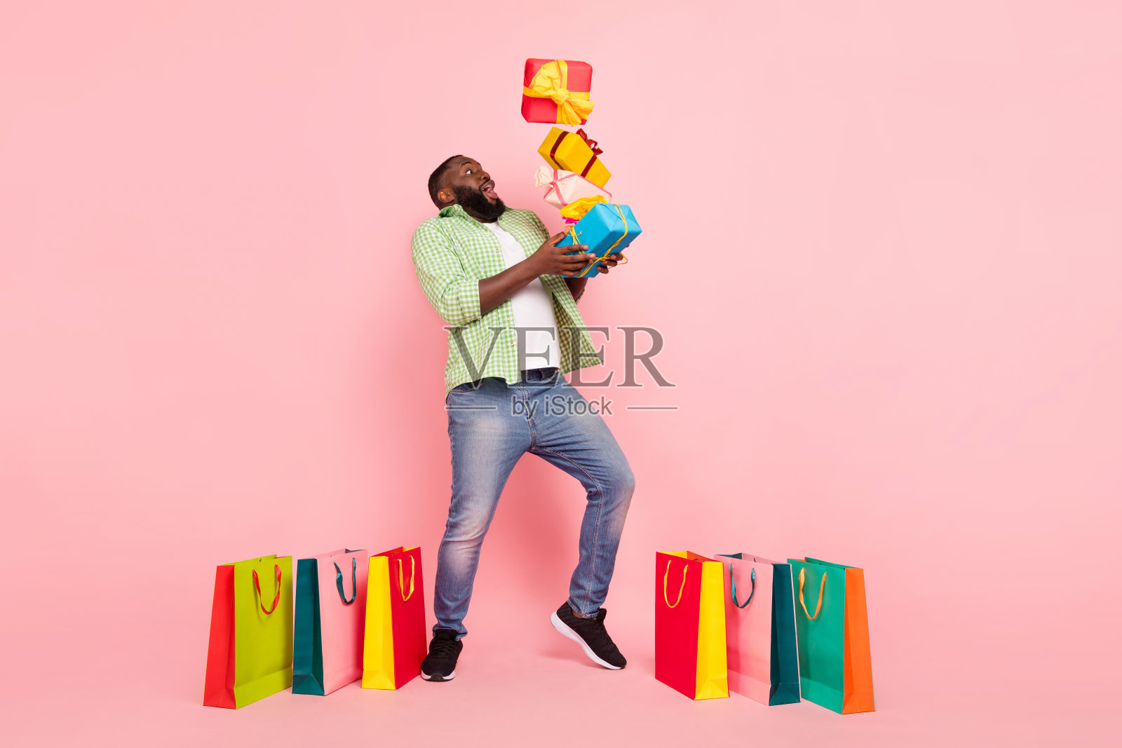 全身照，印象深刻的千禧一代男孩手拿礼物袋，穿着衬衫、牛仔裤和运动鞋，背景为粉色。照片摄影图片