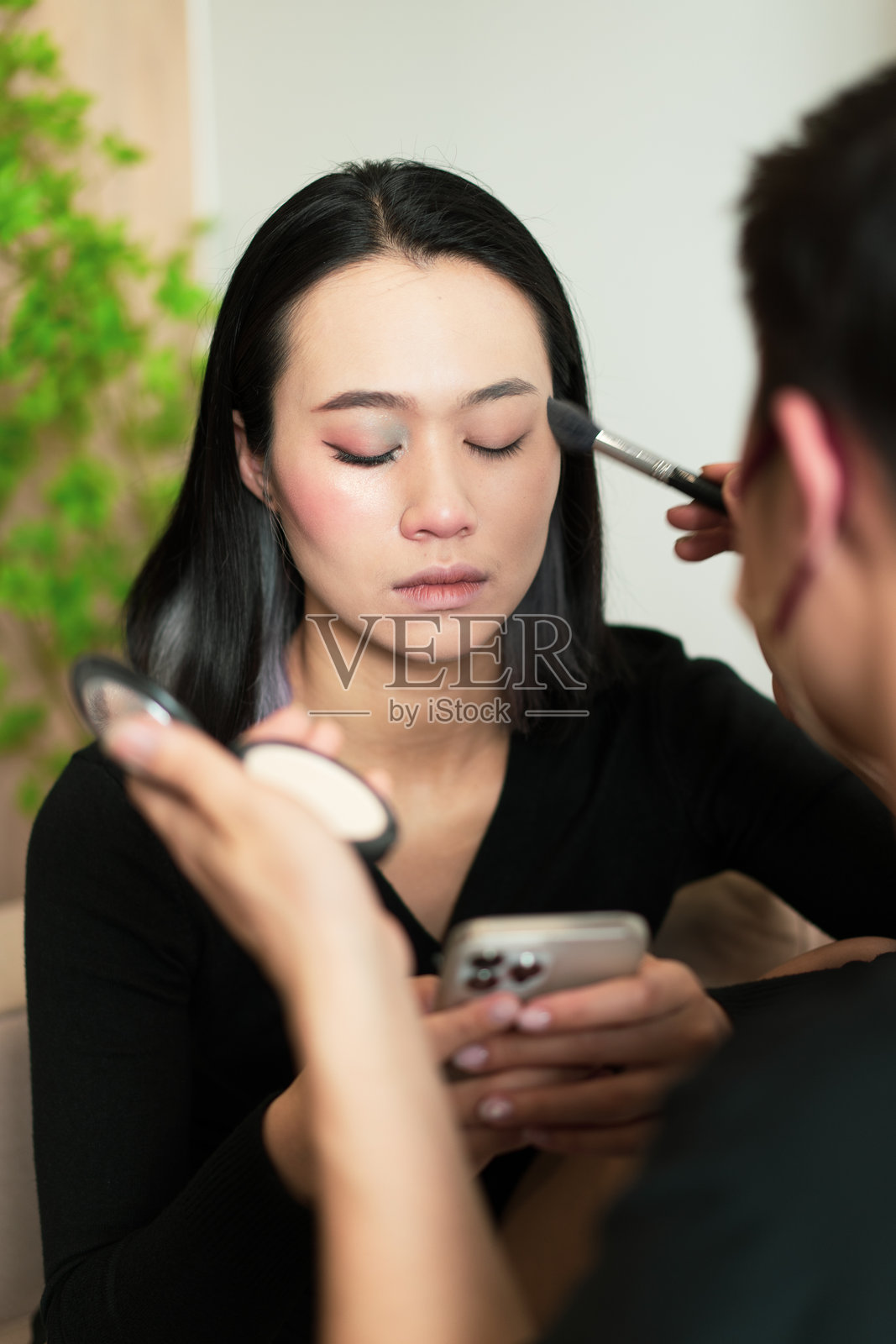 女性在查看智能手机的同时接受化妆服务照片摄影图片