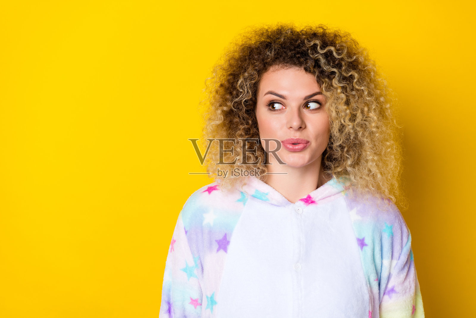 迷人的开朗女孩，波浪卷发，思考中撅嘴，背景为明亮的黄色，留有空白空间。照片摄影图片