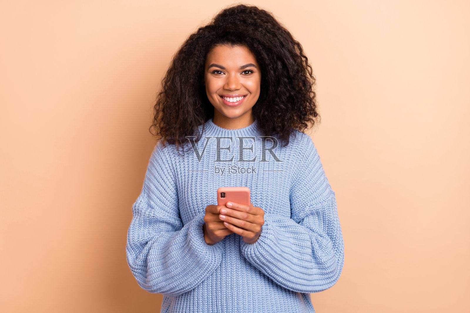 年轻迷人的女性在米色背景下使用手机下载评论应用程序。照片摄影图片