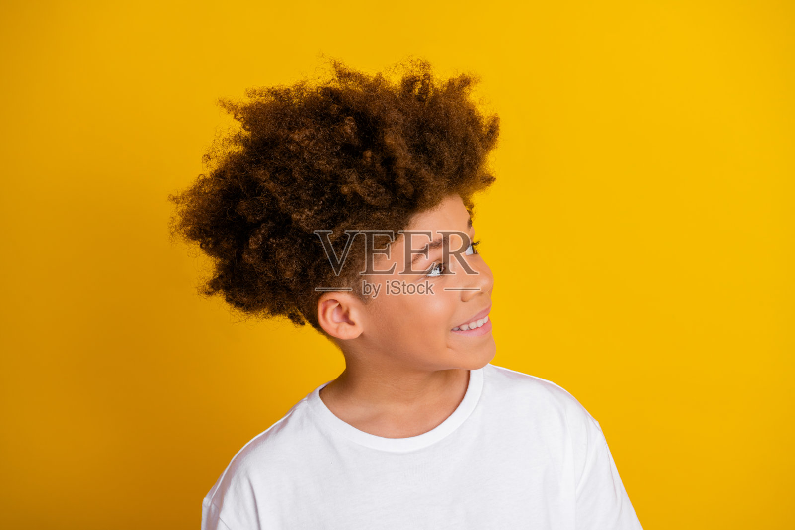 微笑的年轻男孩穿着白色T恤，站在充满活力的黄色背景前，散发着快乐和时尚感。照片摄影图片