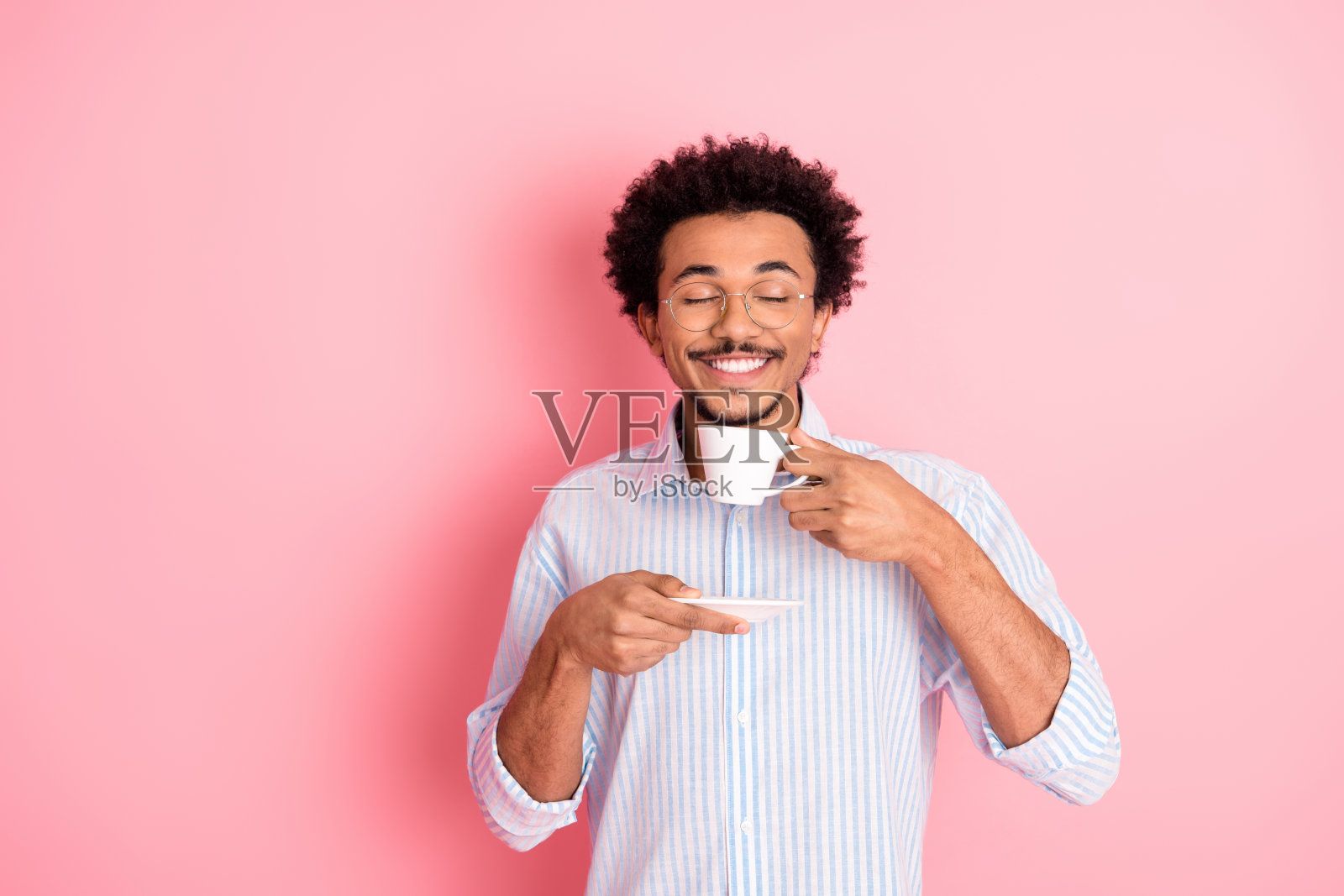 年轻时尚的男士在鲜艳的粉色背景下享受一杯咖啡，悠闲时光中的咖啡品味。照片摄影图片