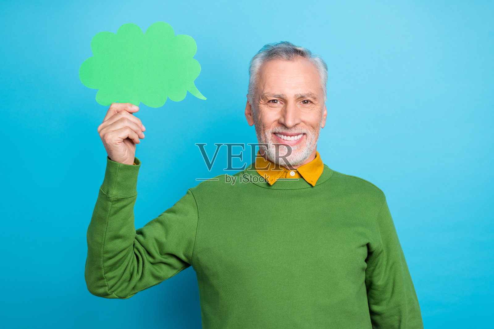 穿着绿色毛衣的幽默快乐退休男士，手持对话气泡，背景为蓝色。照片摄影图片