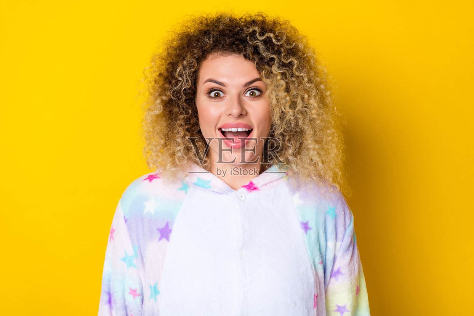 穿着睡衣的迷人、惊讶、快乐的波浪卷发女孩的肖像，心情愉快，背景为明亮的黄色。照片摄影图片