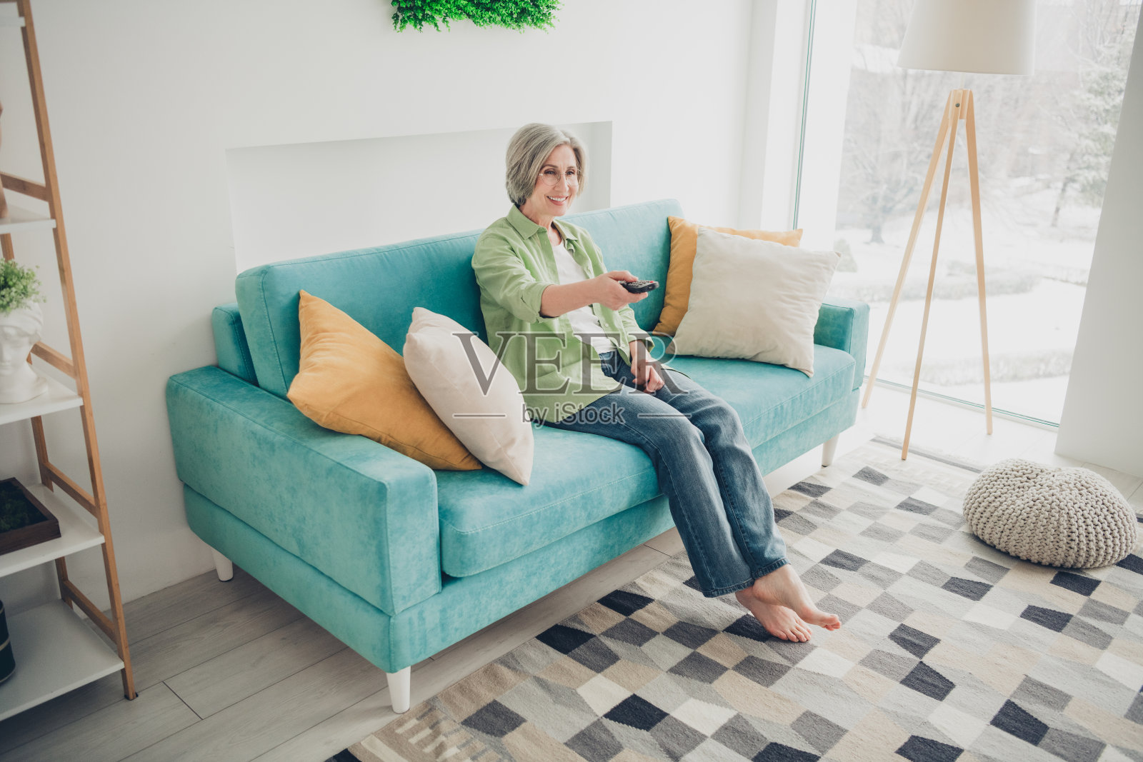 老年女性在现代客厅的舒适沙发上享受悠闲时光，周围装饰温馨。照片摄影图片