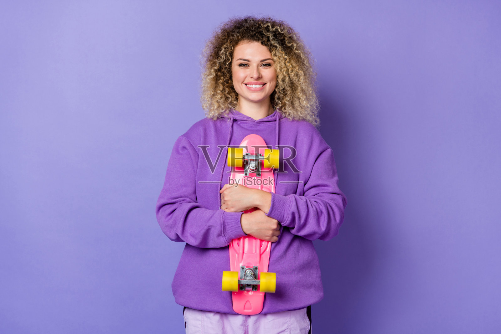 梦幻可爱的女孩穿着连帽衫，拥抱长板，背景为紫色。照片摄影图片